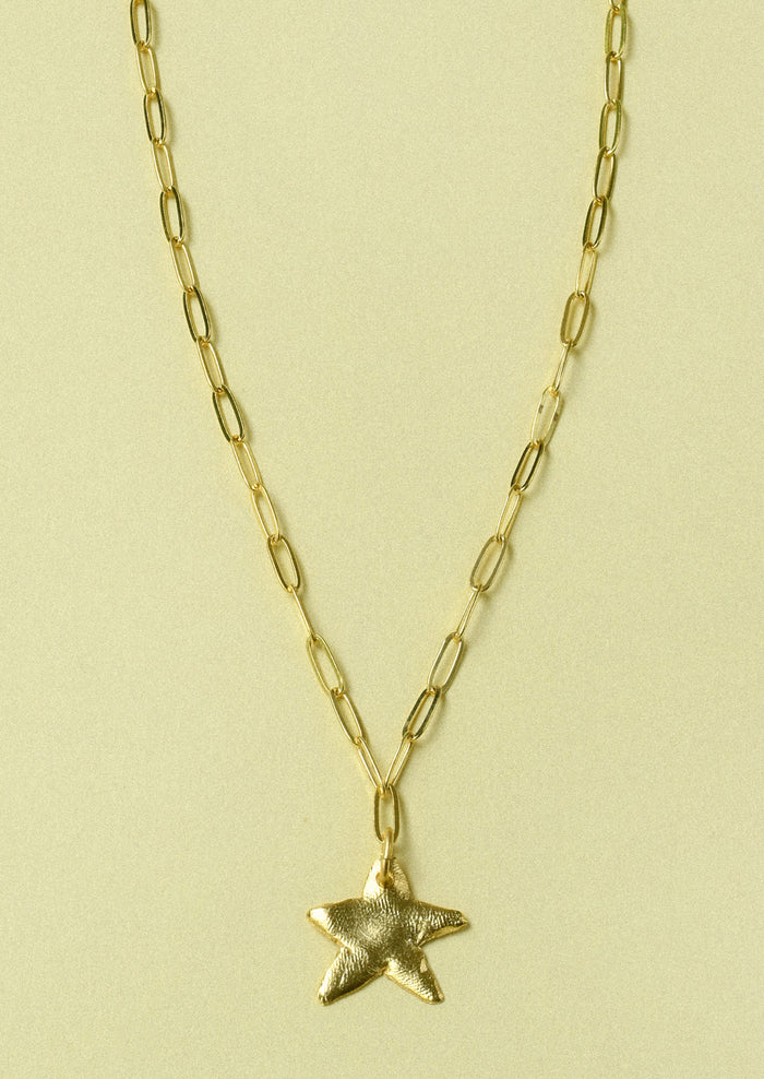 A gold paperclip chain necklace with a large star pendant.