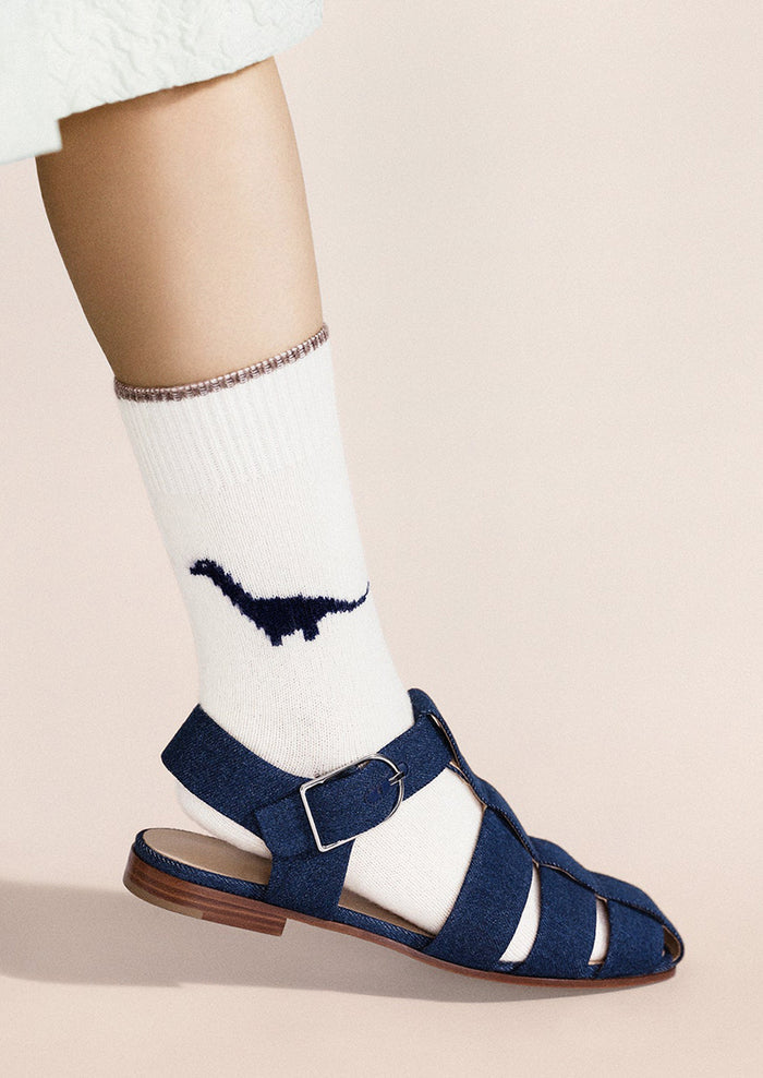 Navy sandals worn with white socks featuring a navy dinosaur design on a beige background