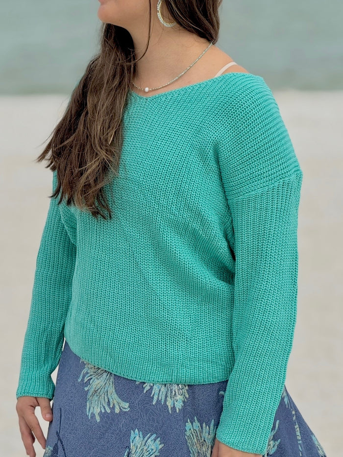 Person wearing a teal sweater with a blurred background